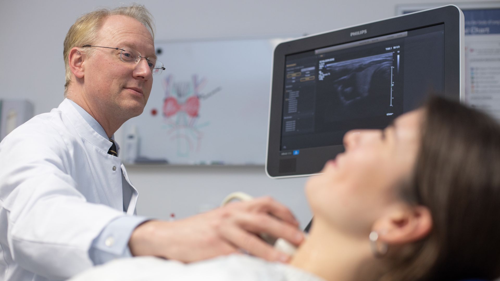Chirurg untersucht per Ultraschall die Schilddrüse einer Patientin