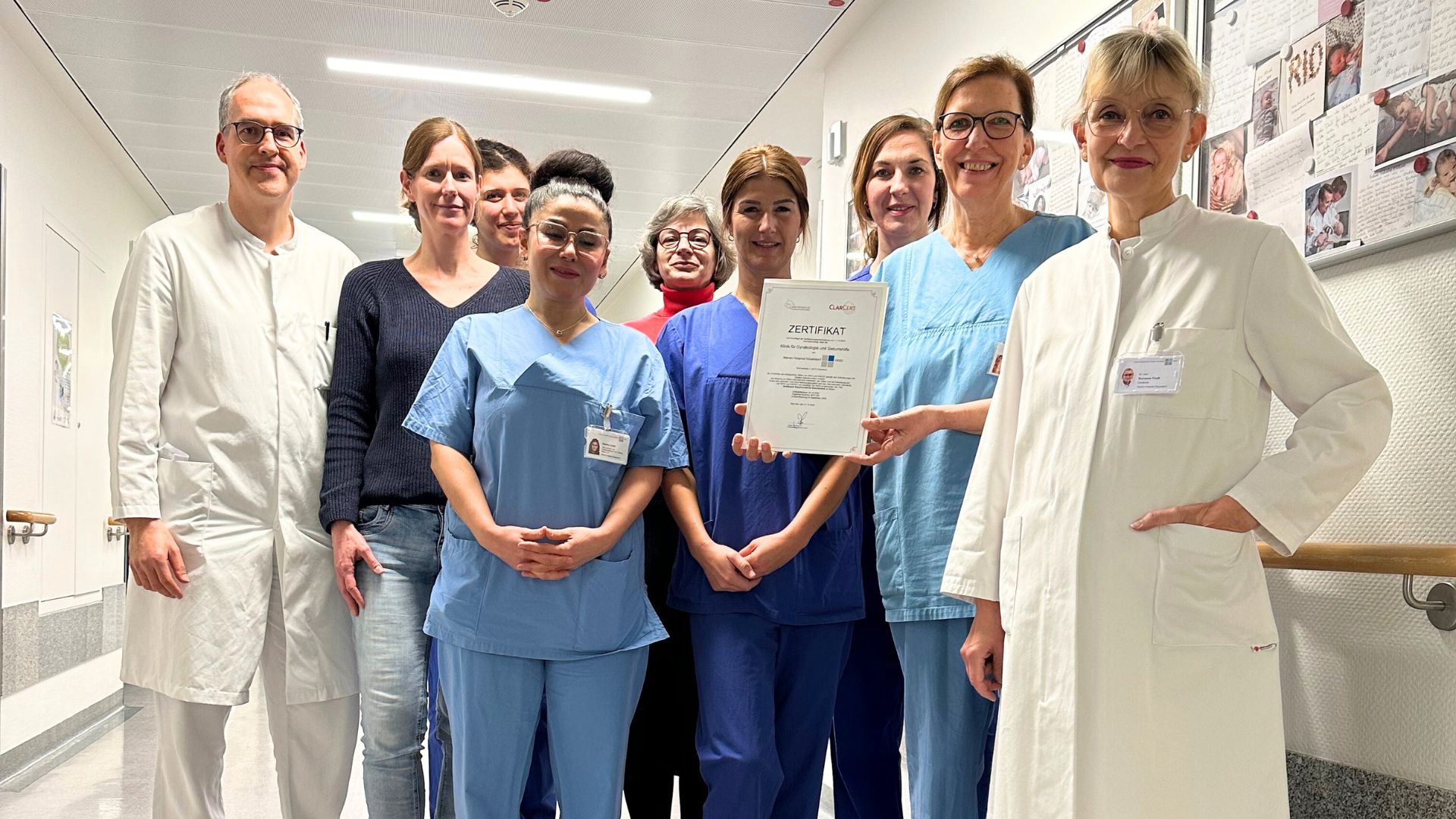 Das ärztliche und pflegerische Team der Geburtshilfe am Marien Hospital Düsseldorf steht im Krankenhausflur und hält das Zertifikat "Babyfreundlich" in die Kamera.